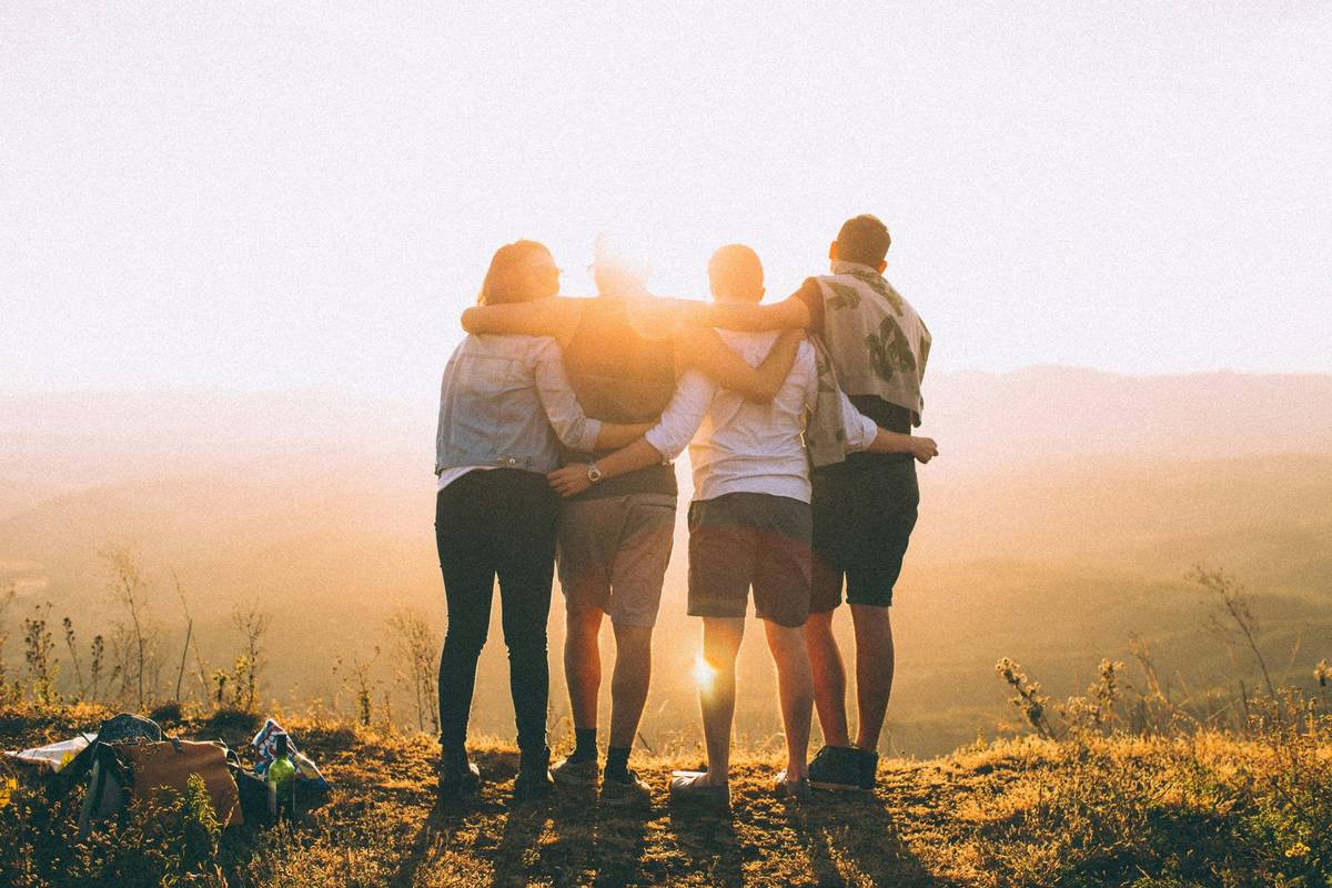Four people with their arms around each other, watching the sun set