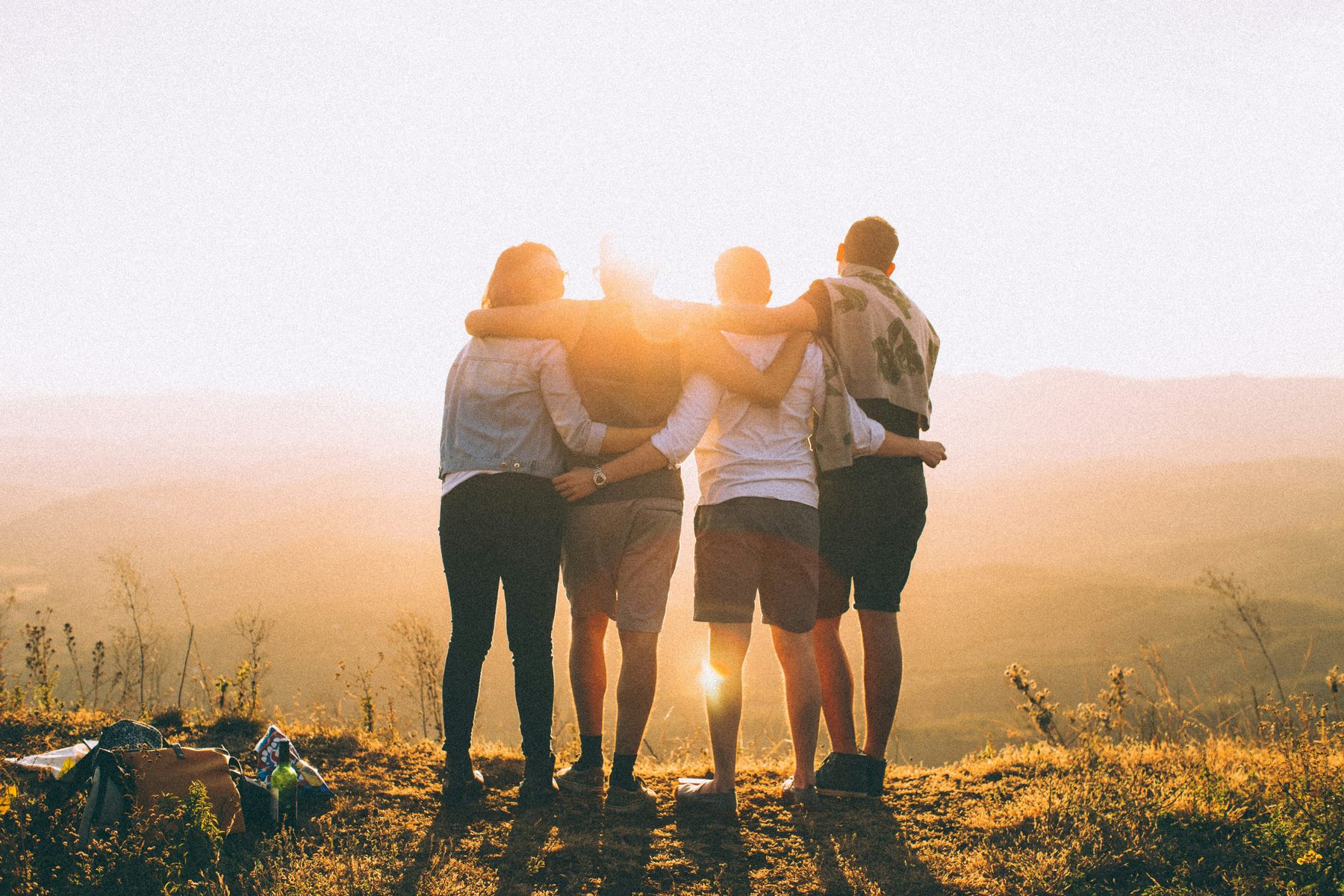 Friends with arms around each other watching the sunset together